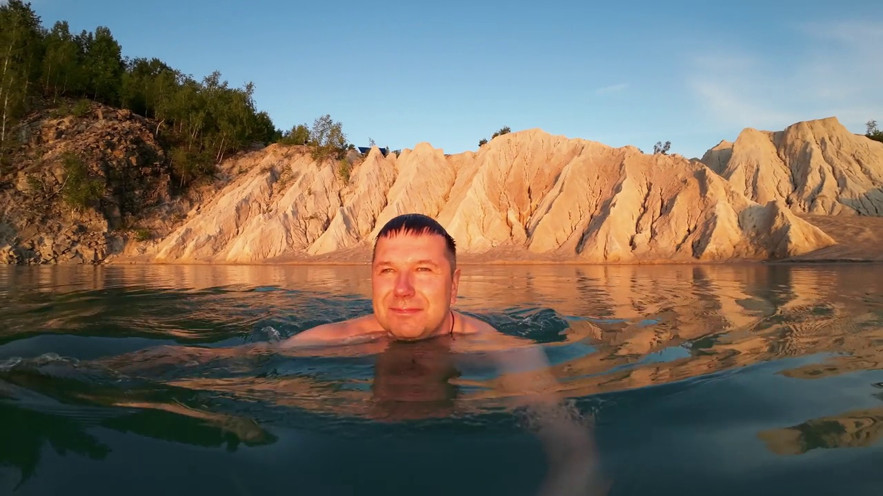 在一个初夏的早晨，一个男人在碧绿的湖水中游泳视频素材