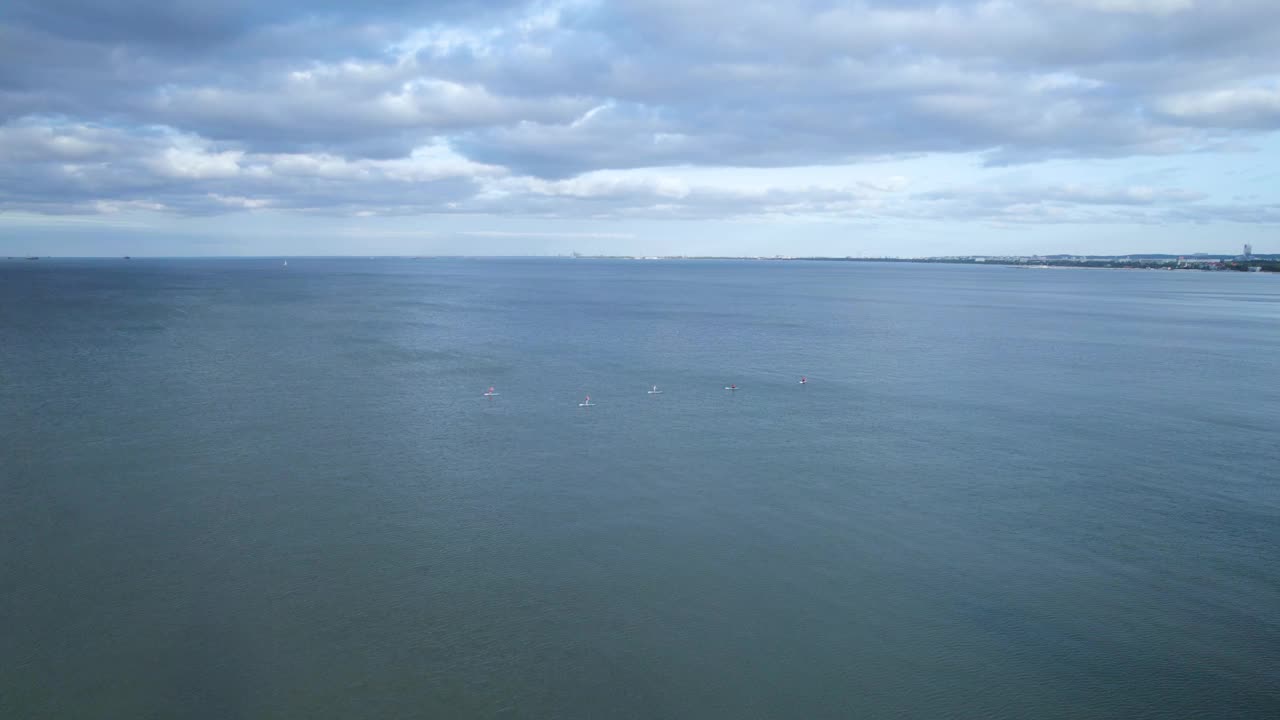 海上直立桨板上的群的无人机视图。在阴天的夏天，人们在红色桨板上旅行视频素材