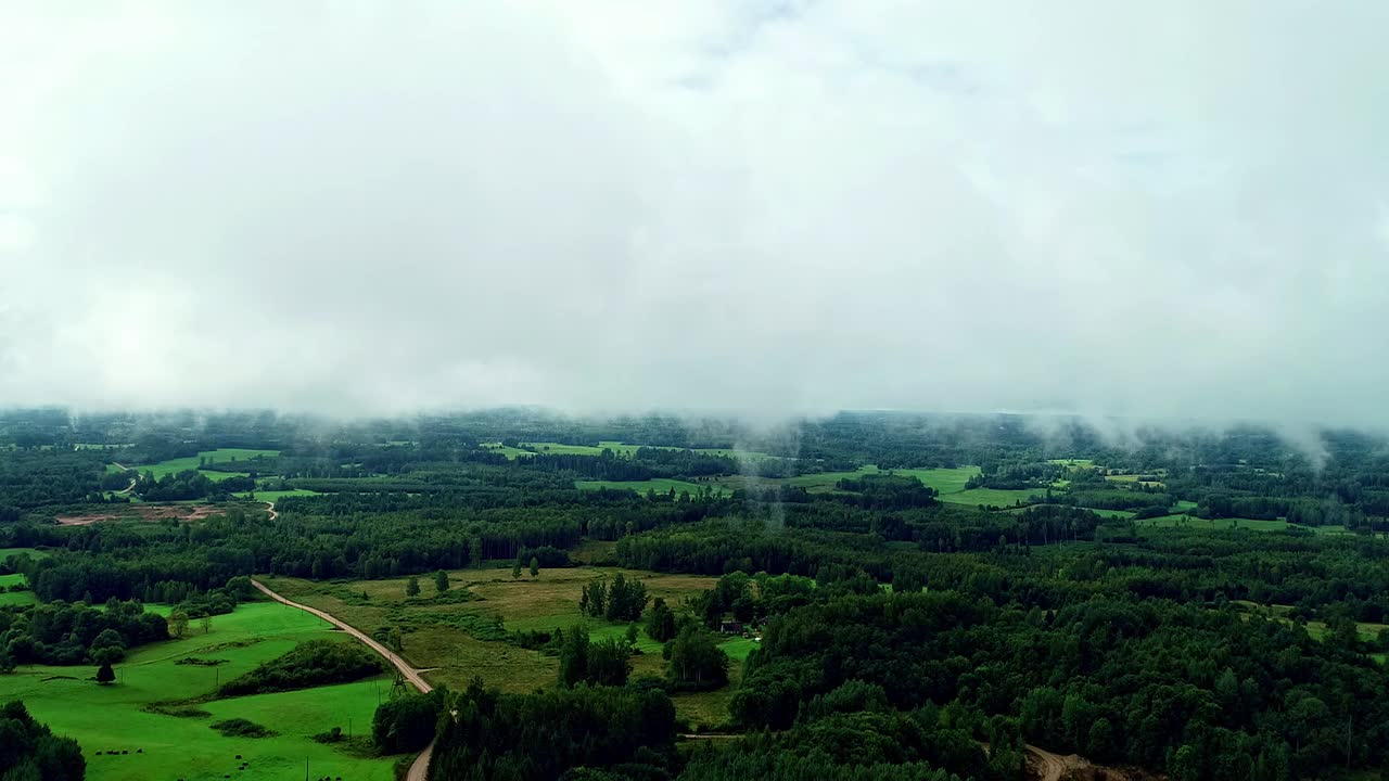 空中无人机拍摄的美丽运动的蓬松的云在白天。云彩漂浮在绿色乡村景观和砾石道路上的镜头。视频素材