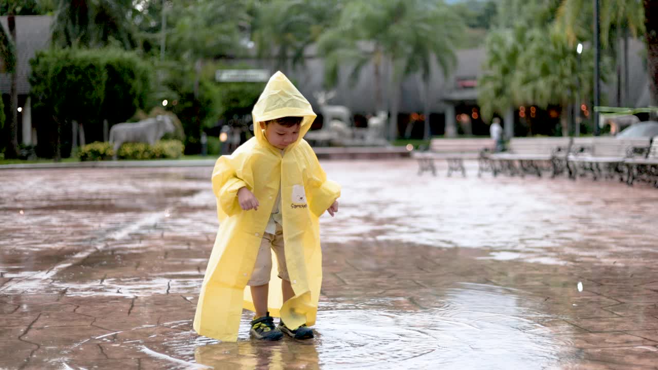 可爱的小男孩在下雨天玩耍，小男孩在户外散步，在水坑上跳跃视频素材