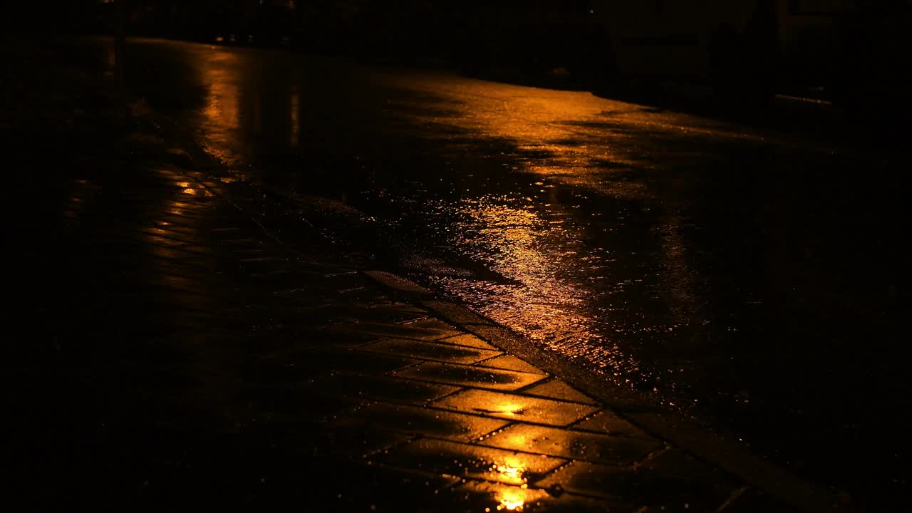 夜雨和雨滴落在水坑里。倾盆大雨和灯火通明的水坑。视频素材