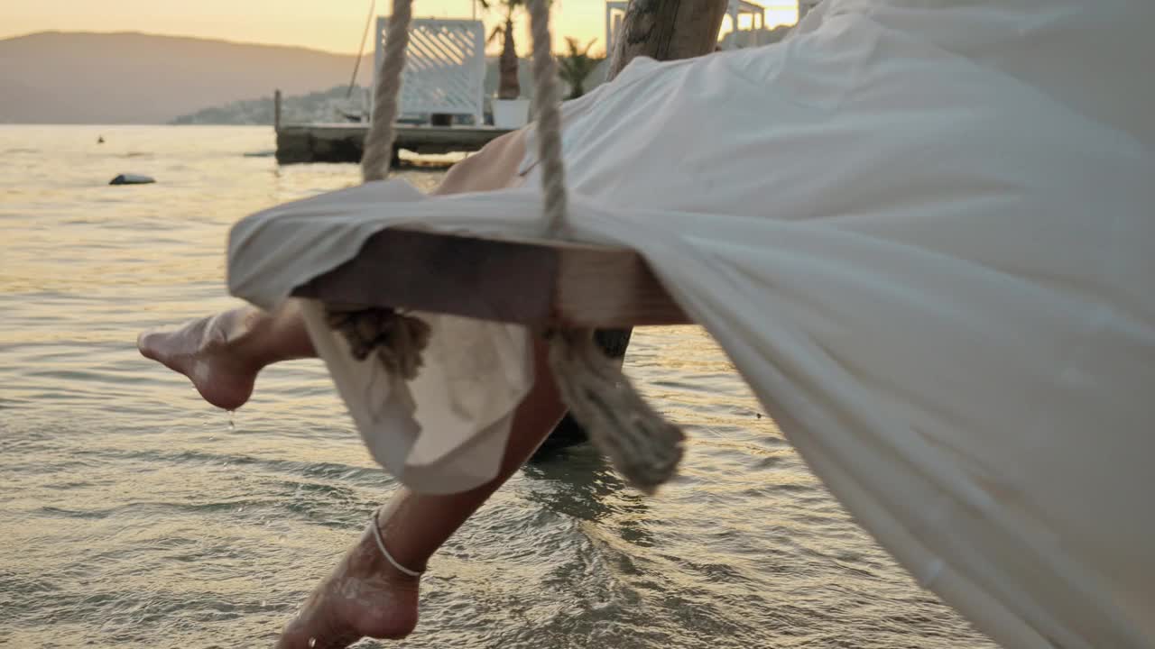 日落时分，一名身穿优雅长裙的女子在海边的秋千上。旅游的精髓，夏日的魅力，自由的感觉，旅行的冒险。视频素材