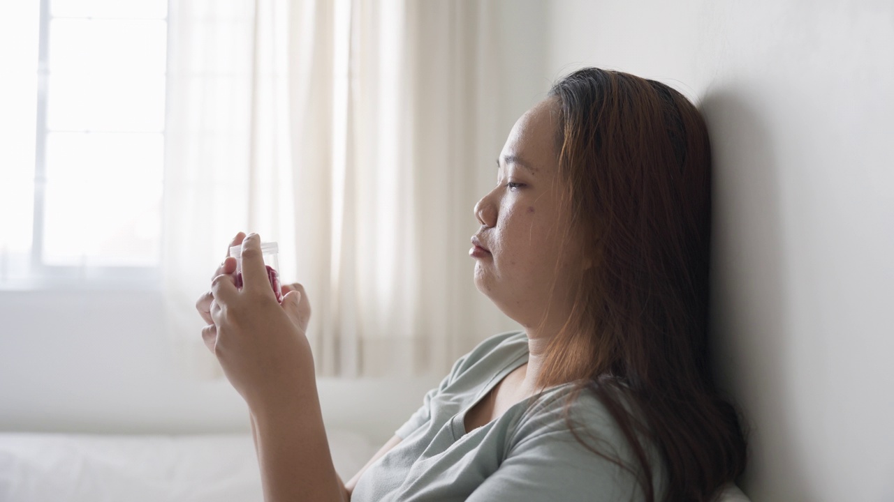 忧心忡忡的沮丧的生病的女人拿着药瓶躺在床上视频素材