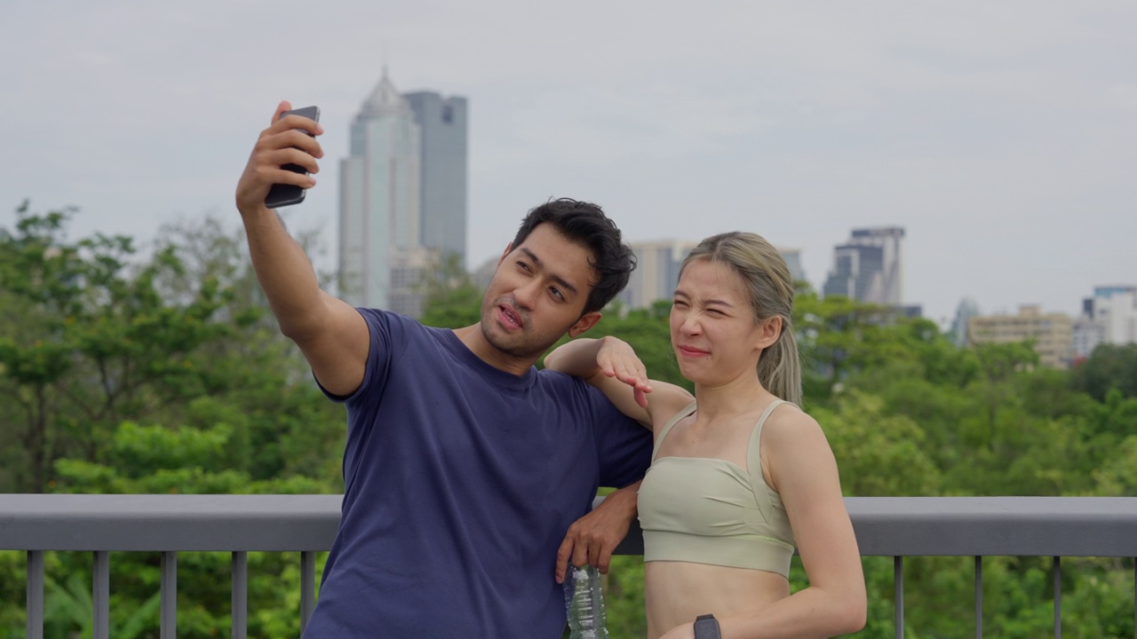 一对年轻的亚洲夫妇在市中心的一个公园里一起慢跑后用智能手机自拍。视频素材