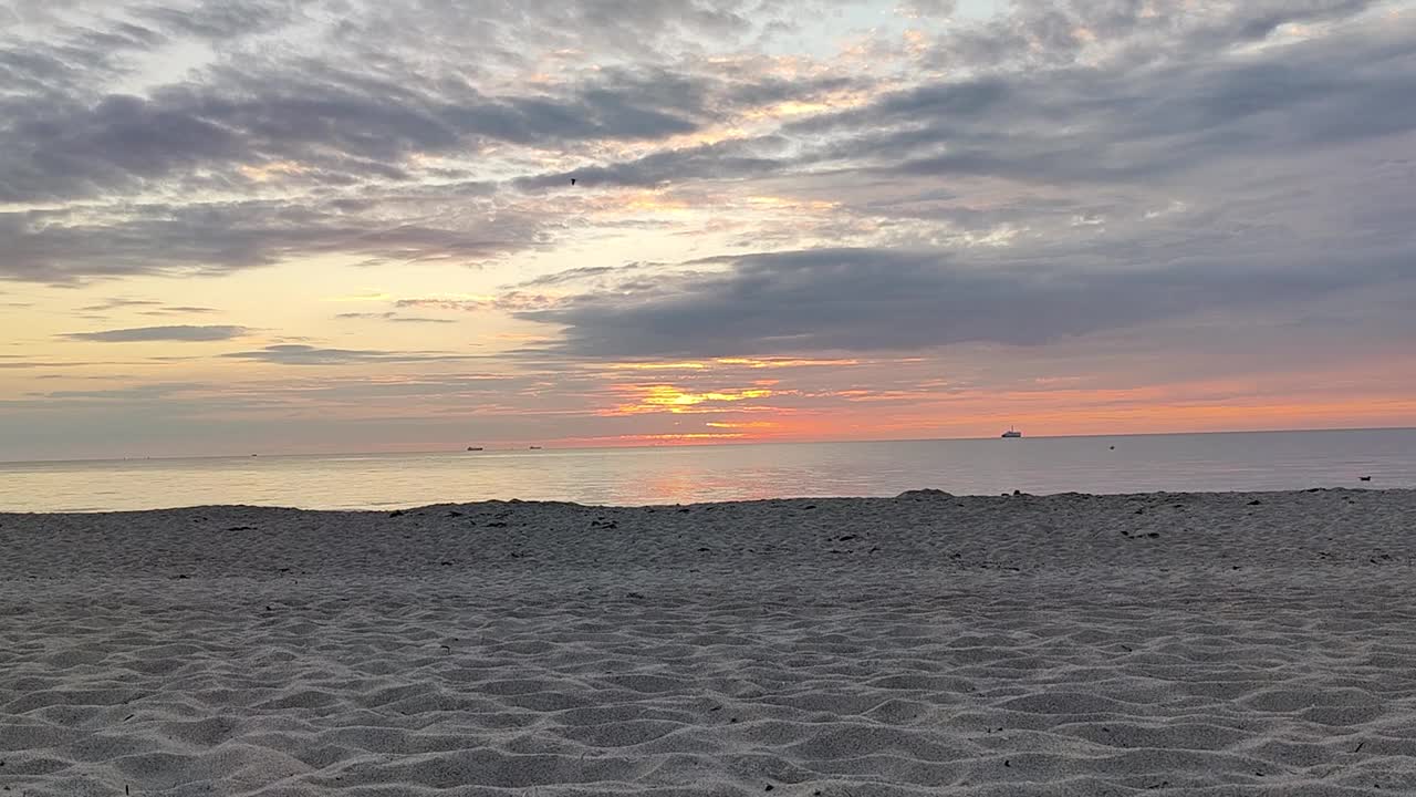 波罗的海的日落，背景是过往的船只，前景是沙子视频素材