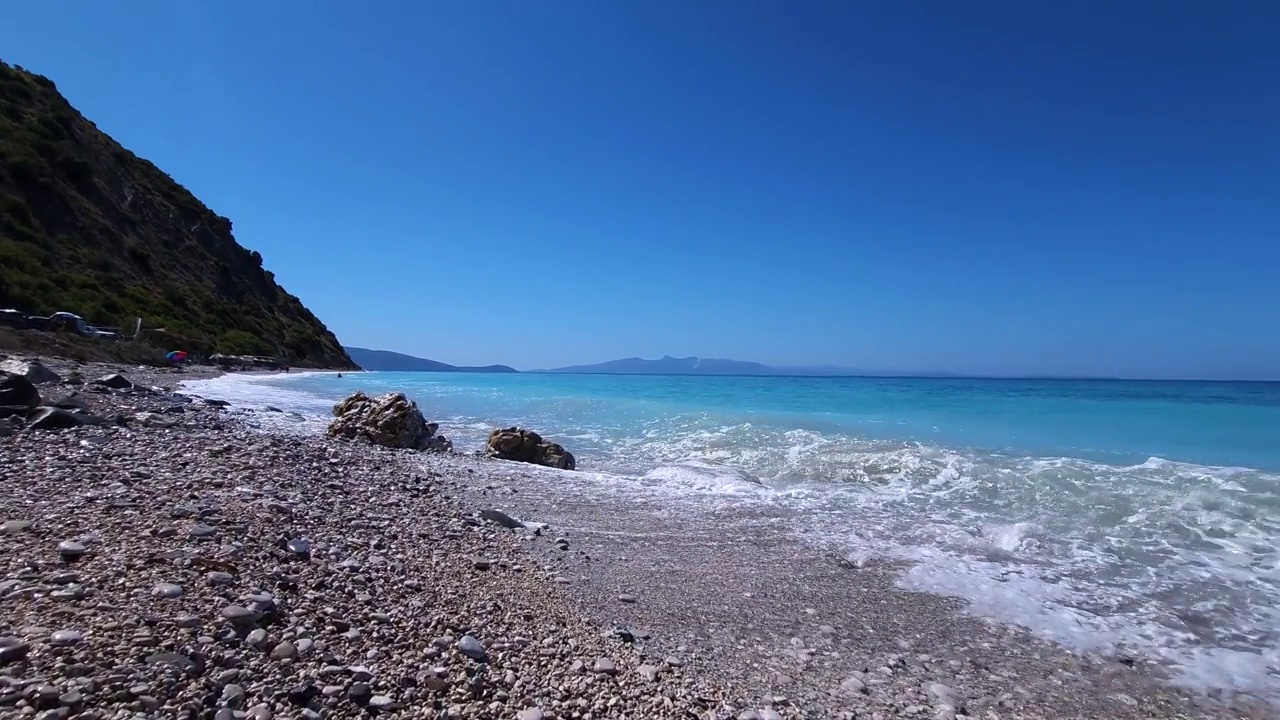 漫步在天堂海滩的鹅卵石被白色的海浪冲刷着，美丽的海边有山和蓝色的绿松石海水在阿尔巴尼亚视频素材