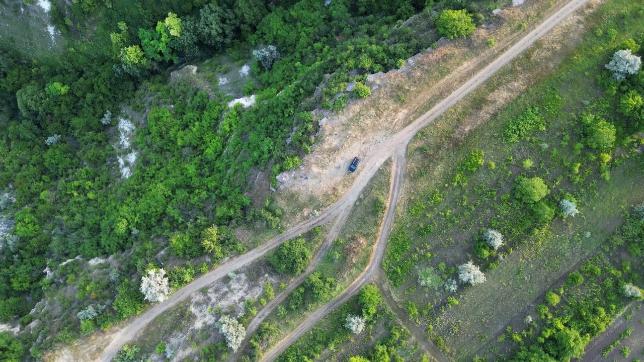 无人机空中盘旋在乡村道路和绿色田野附近的岩石地区，发现孤独的黑色汽车，4K视频素材