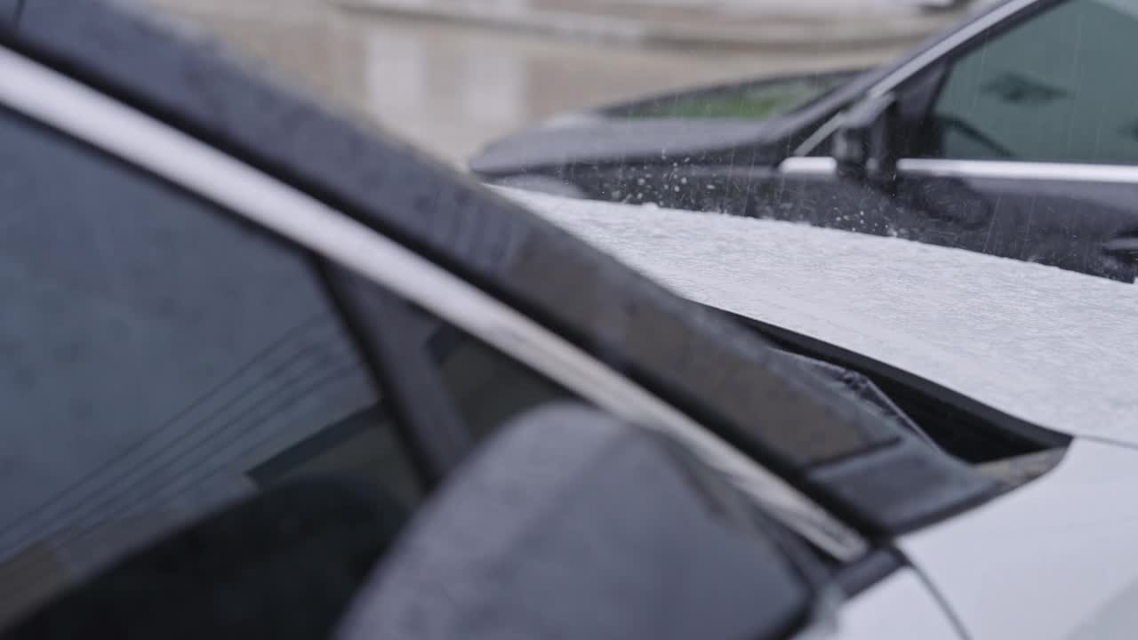 SLO MO:大雨落在两辆停在住宅楼前的汽车上，在暴风雨的日子里，黑色的汽车挡住了白色的汽车，白色的建筑反射在汽车的窗户上。视频素材