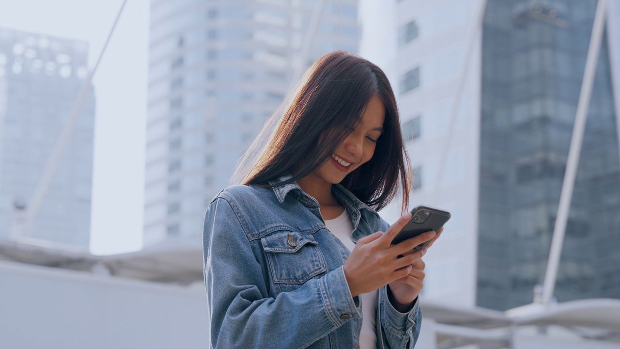 年轻的亚洲女子站在城市里，在街上使用手机视频素材