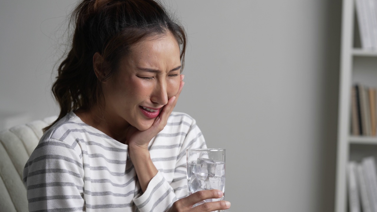 年轻的亚洲女子在喝装有冰块的水时牙痛。医疗保健理念。视频素材