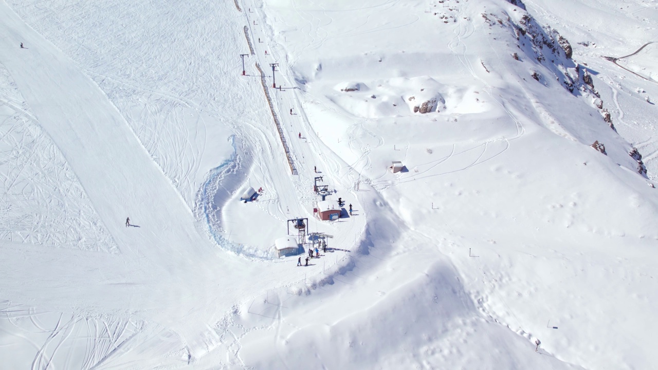 鸟瞰冬季游客在陡峭的积雪覆盖的山坡上开始登上滑雪场缆车视频素材