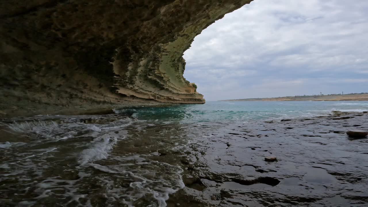 在马耳他的一个洞穴里，平静的绿松石水缓缓地流过平坦的岩石表面。视频素材