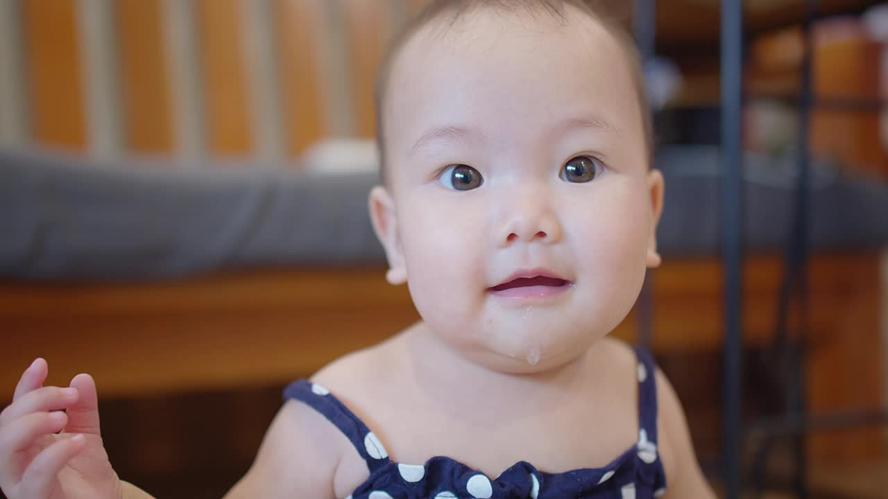 肖像特写快乐可爱可爱的小亚洲婴儿学步儿童女孩看着和微笑的镜头，而躺在家里的客厅视频素材