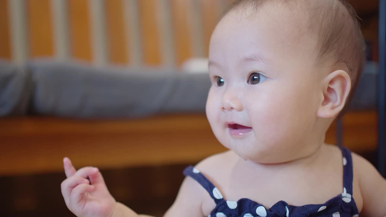 肖像特写快乐可爱可爱的小亚洲婴儿学步儿童女孩看着和微笑的镜头，而躺在家里的客厅视频素材