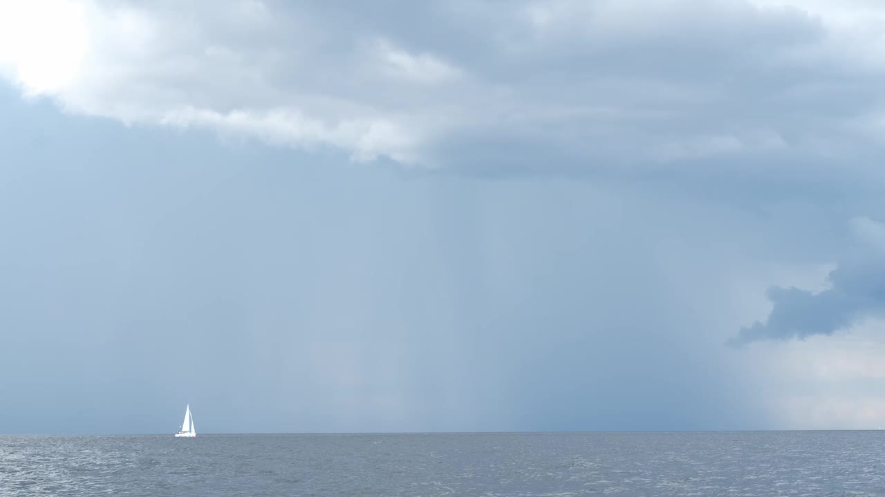 天边下着雨，灰色的雨云和白色的帆船驶向大海，刮风的天气，雷雨，暴风雨。视频素材