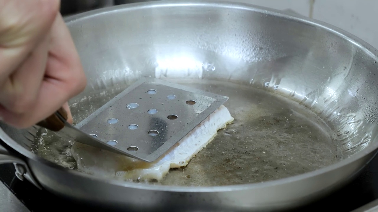 在厨房烤鱼。厨师正在用煎锅煎鱼的特写，厨师正在厨房里做饭，用煎锅煎鱼，在餐馆里准备食物。视频素材