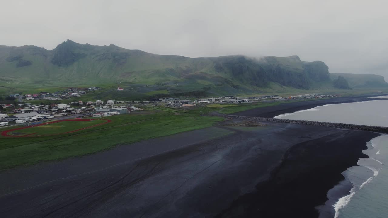 轨道无人机拍摄到美丽的蓝色海浪冲击着冰岛维克前的黑色沙滩，以及远处巨大的岩层和山脉视频素材