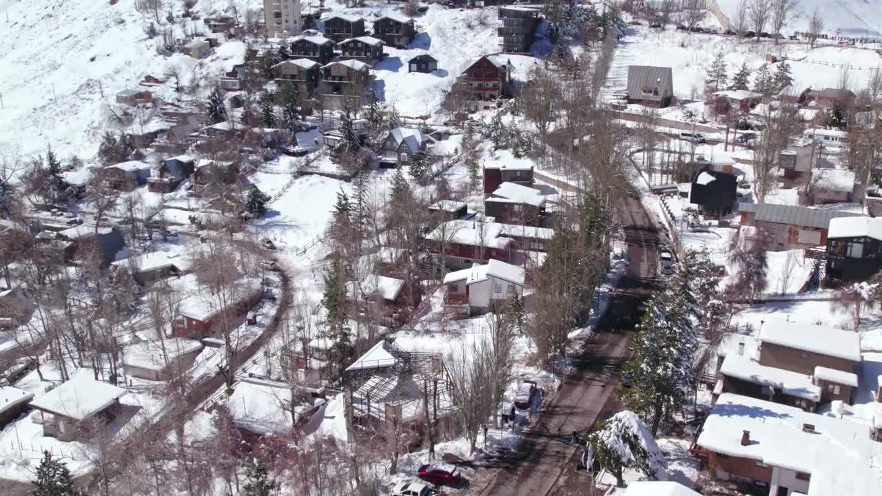 在智利圣地亚哥附近的一个山区旅游村庄Farellones的街道上空，空中轨道上，满是乘客的面包车穿过白雪覆盖的街道，北欧风格的小屋。视频素材