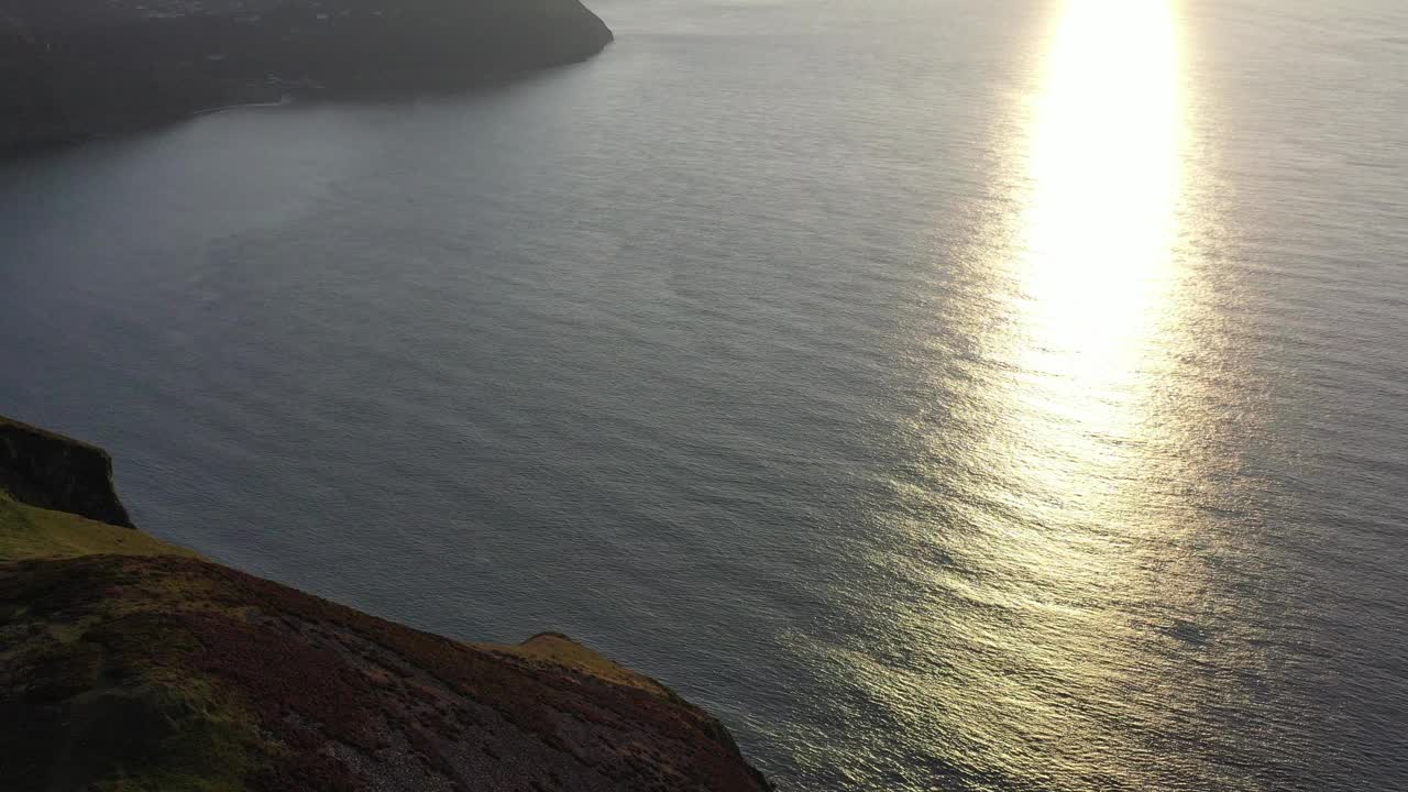 在北德文郡海岸观看日落时太阳光线在海洋上的反射时，无人机倾斜拍摄，俯瞰英国的林顿和林茅斯。视频素材