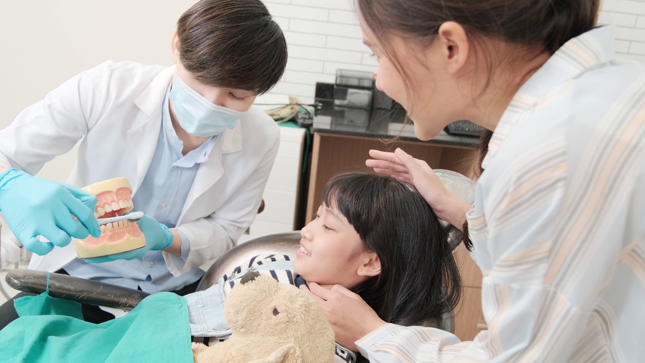 一位亚洲女牙医在牙科诊所向一个女孩展示牙刷。视频素材