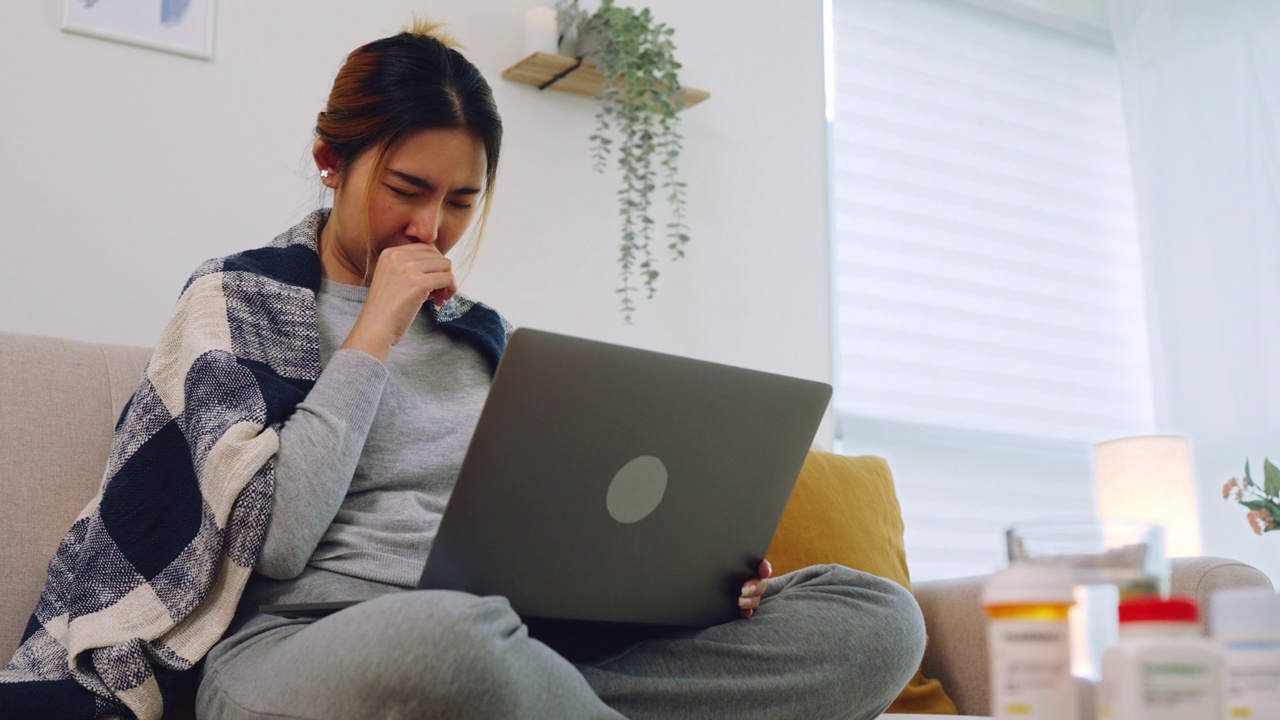 一名亚洲妇女在家里的客厅里通过远程医疗与医生进行视频通话，感染了流感病毒视频素材