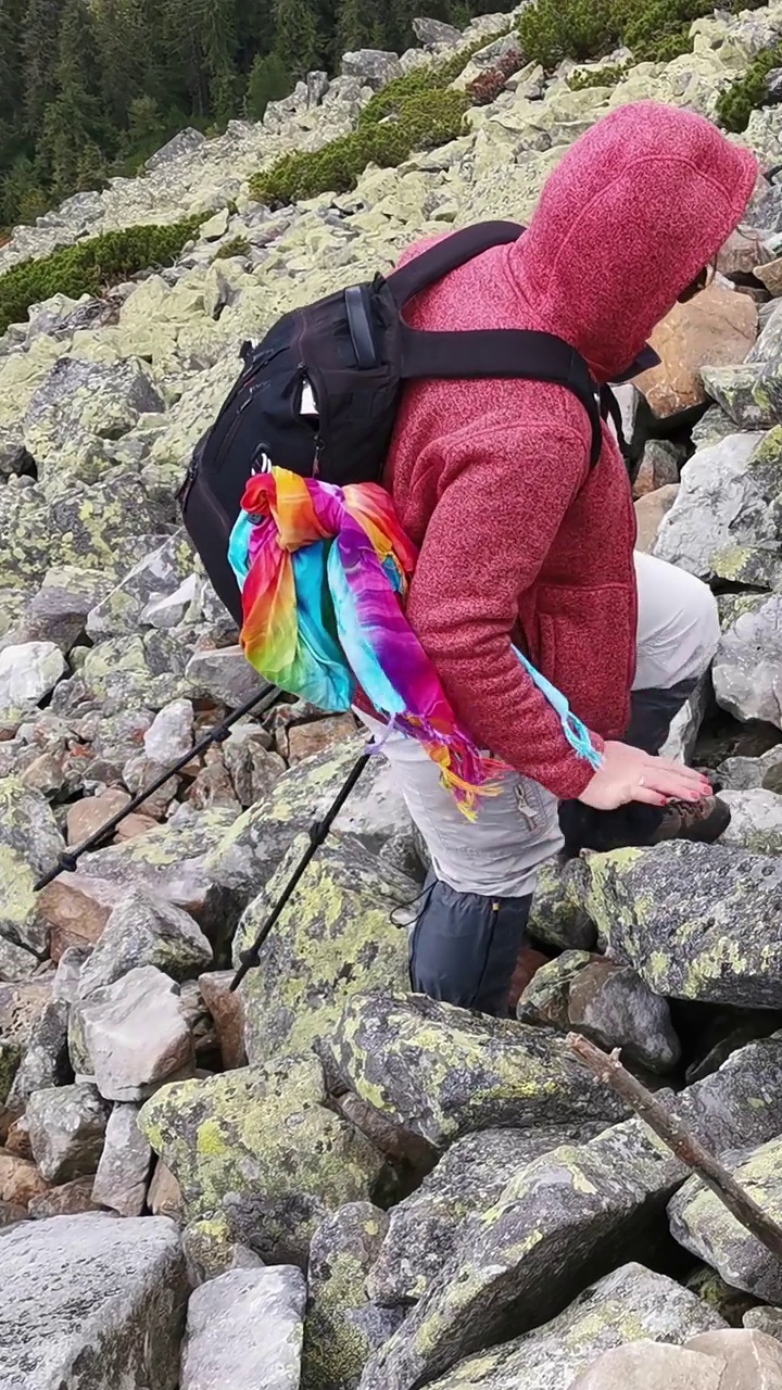 一位手持登山杖的妇女在登山途中爬上一条岩石小径视频素材