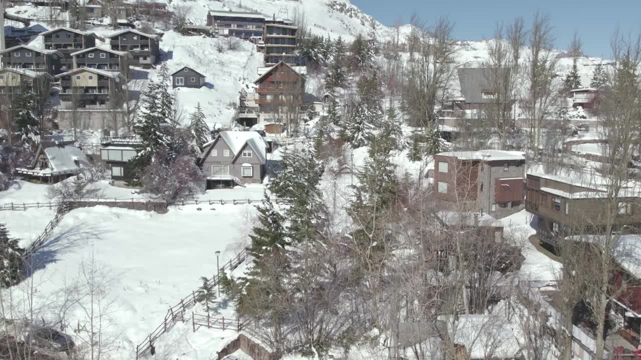 在智利的一个阳光明媚的日子里，在雪覆盖的Farellones山村，鸟瞰小屋和豪宅附近。视频素材