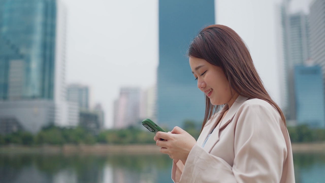 快乐的年轻亚洲女性一边在智能手机上打字，一边走在户外看城市街景。漂亮的年轻女子喜欢用手机在户外散步。生活方式的概念视频素材