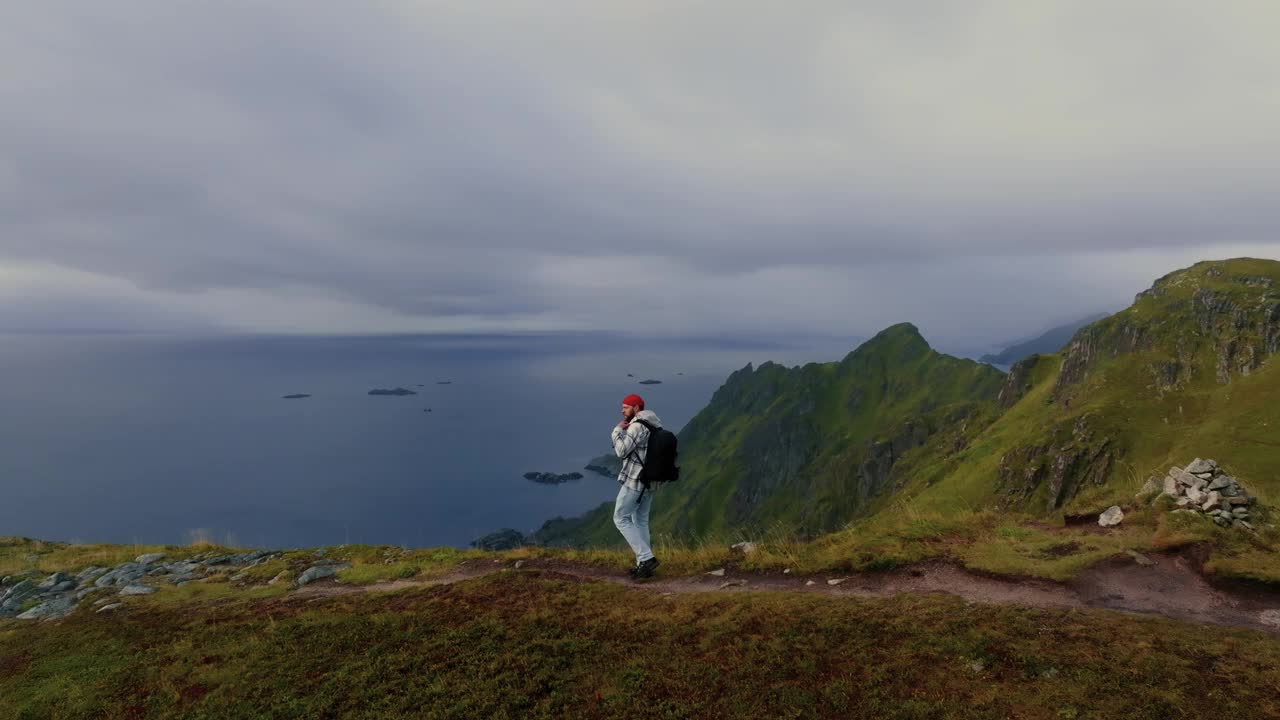 年轻的男性旅行者走向悬崖边缘，欣赏罗弗敦群岛的壮丽景色视频素材