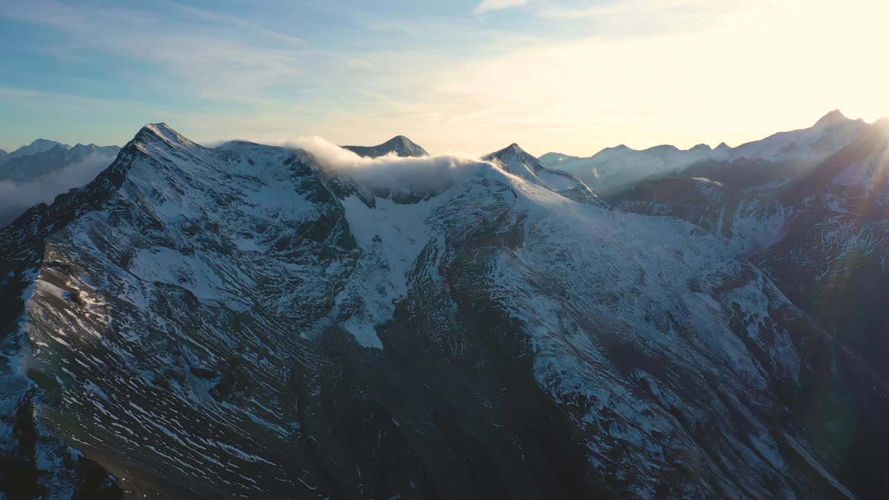 黄昏鸟瞰白雪覆盖的阿尔卑斯峰顶与夕阳的光束，奥地利的霍赫陶恩国家公园视频素材