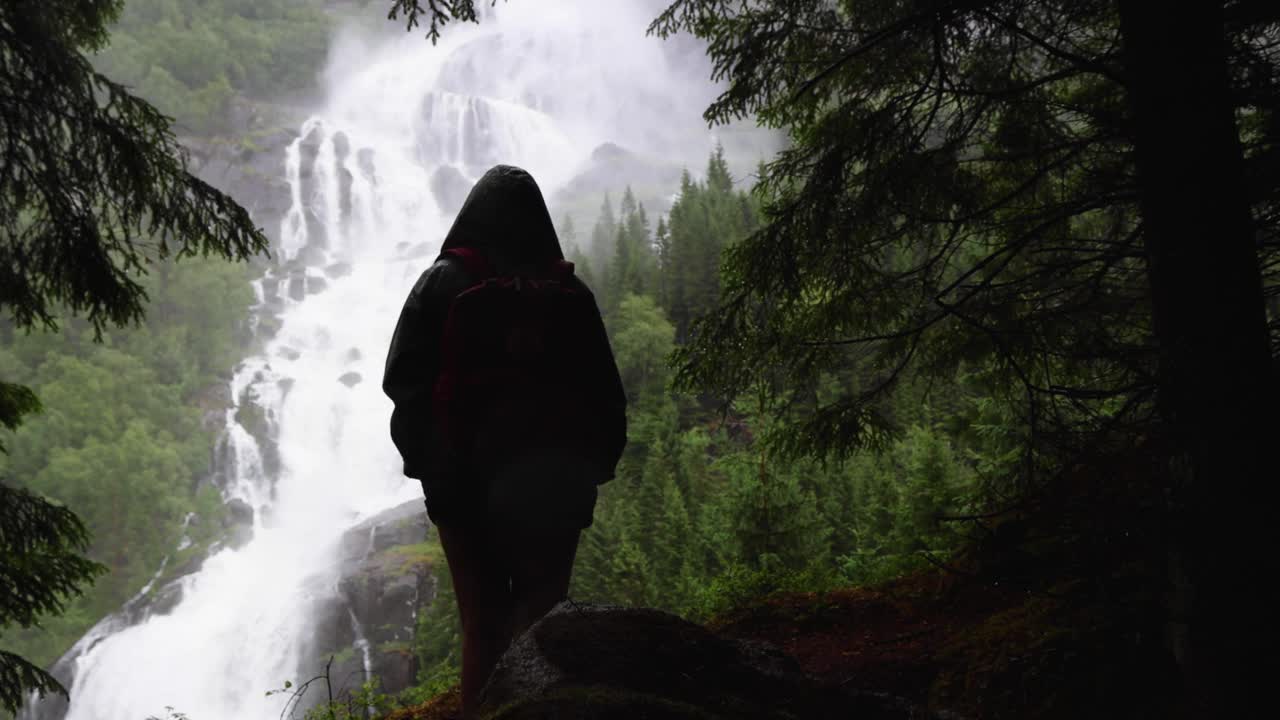 多云雨天的Tjornadalsfossen瀑布，周围环绕着挪威的绿色松林。水从陡峭的山上流下来，在忧郁的一天和徒步旅行者一起制造薄雾。视频下载