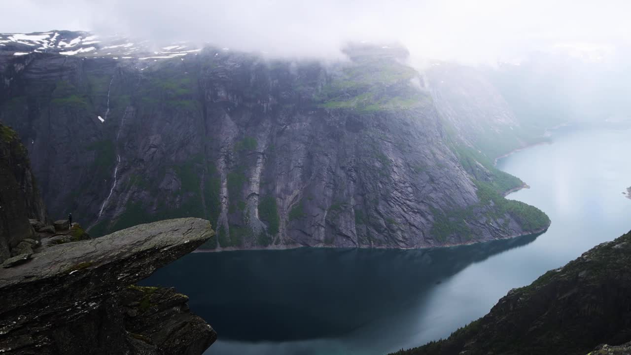 从Trolltunga俯瞰蓝色的挪威峡湾，周围群山环绕，陡峭的悬崖和多云的瀑布。视频下载