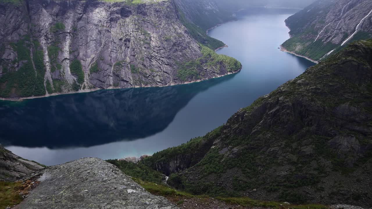 从Trolltunga俯瞰蓝色的挪威峡湾，周围群山环绕，陡峭的悬崖和多云的瀑布。视频素材