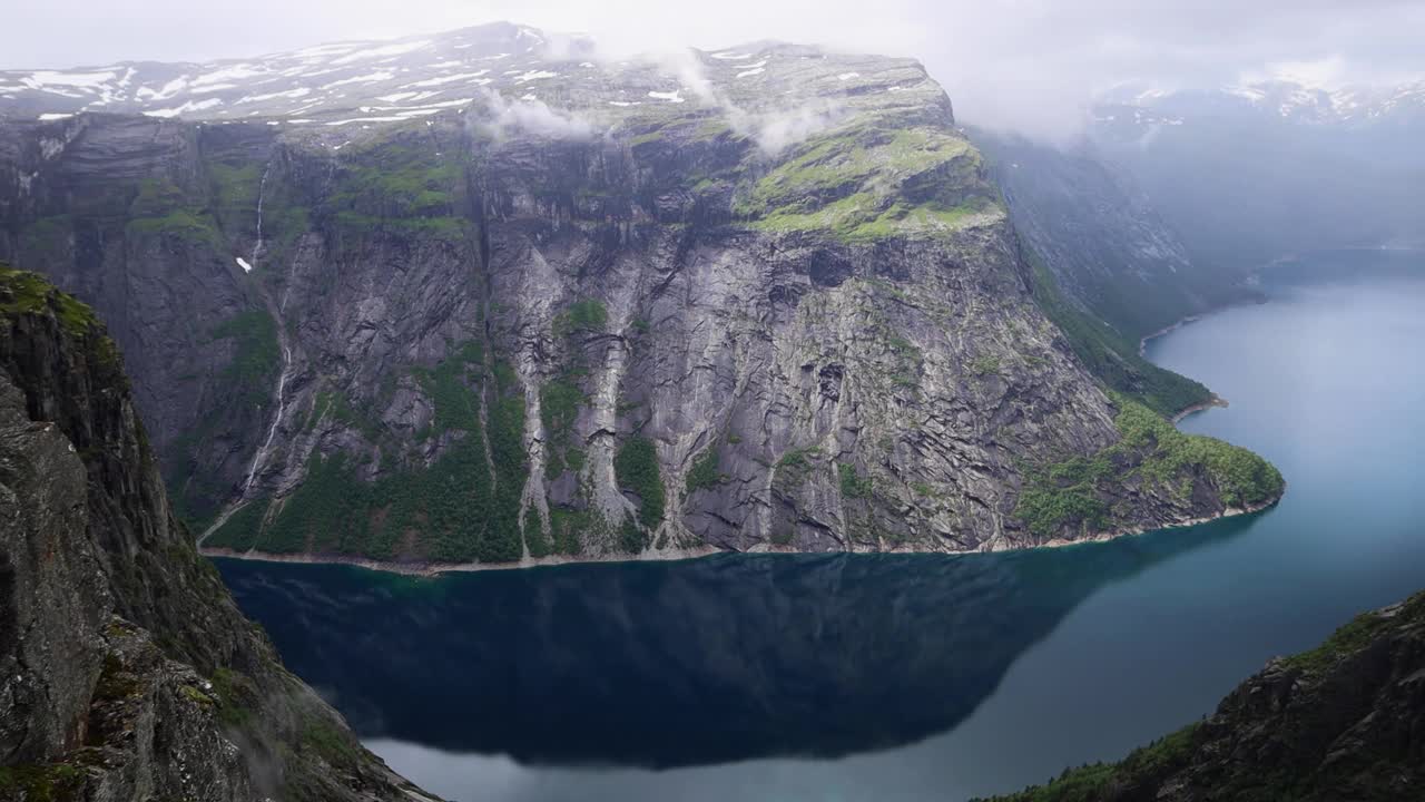 从Trolltunga俯瞰蓝色的挪威峡湾，周围群山环绕，陡峭的悬崖和多云的瀑布。视频下载