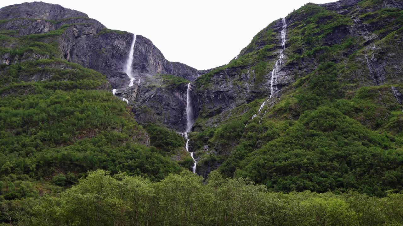 高大的瀑布从山顶落下，周围是陡峭的悬崖和松树林，挪威。视频下载