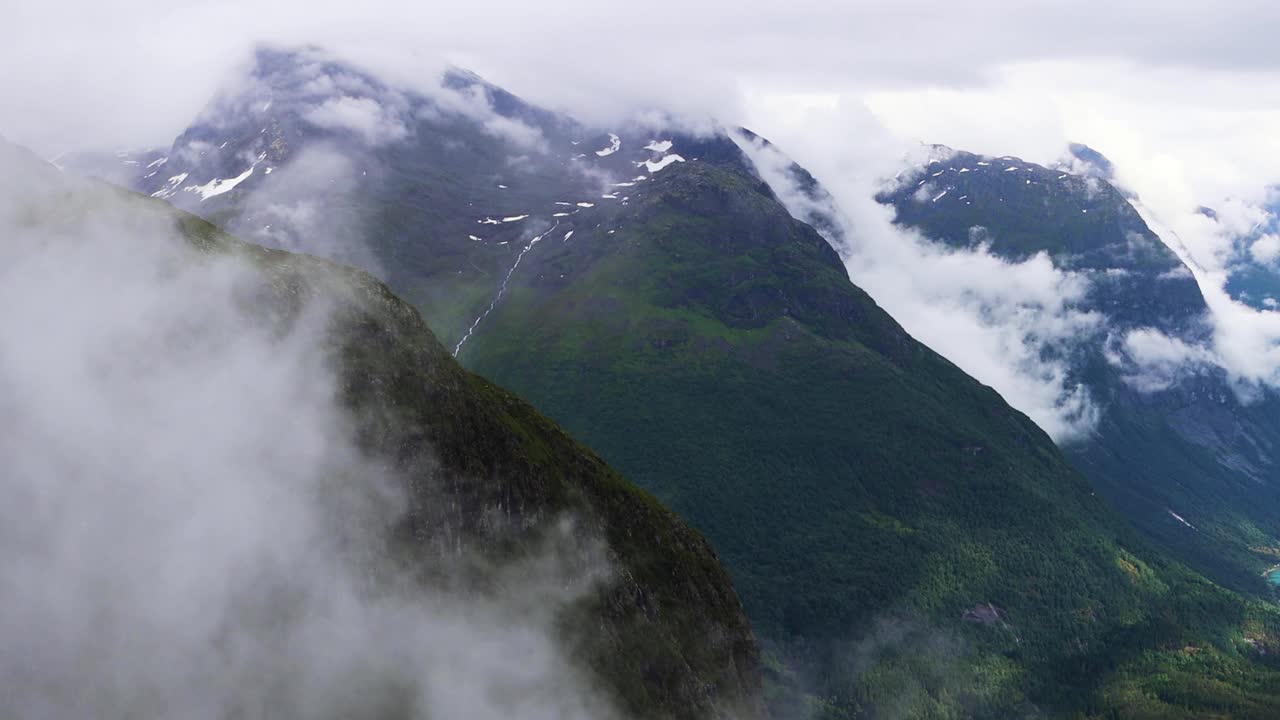 挪威洛瓦内特山谷的高大山脉被云层包围，笼罩在明亮的蓝色冰川湖上。雾天的大气景观。视频下载