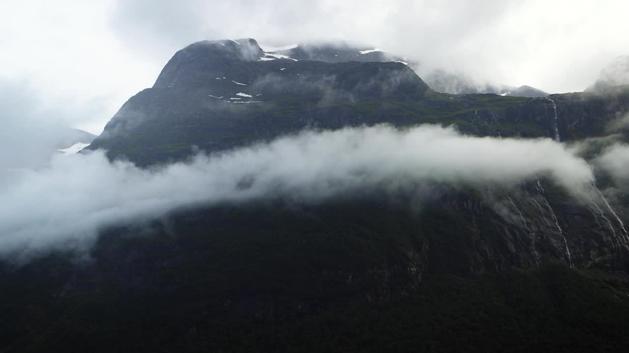 挪威洛瓦内特山谷的高大山脉被云层包围，笼罩在明亮的蓝色冰川湖上。雾天的大气景观。视频下载