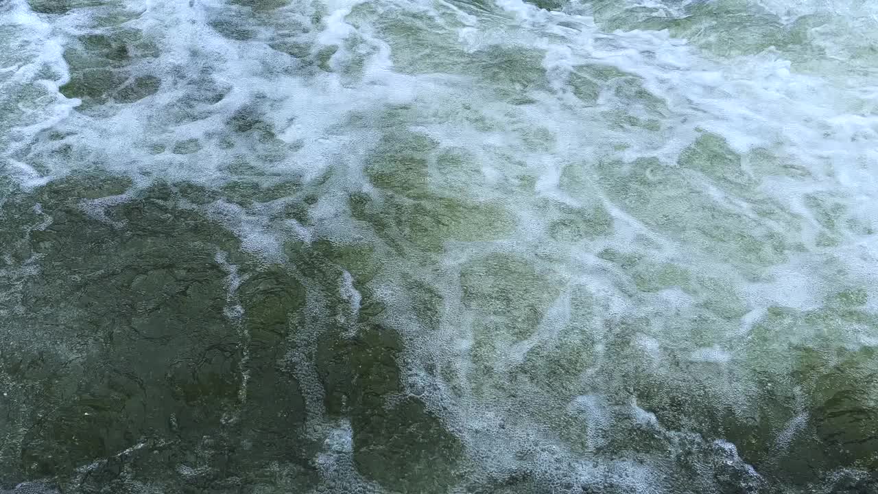 一条清澈的小溪，汩汩的水流过巨石。一条大河从石头上流过。夏日里，山间湍急的河水溅起水花。视频下载