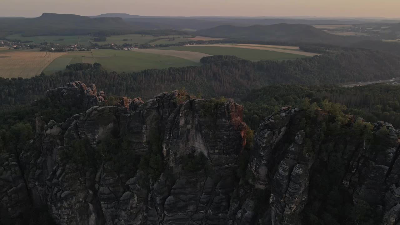 令人惊叹的户外景观，前景是一个巨大的岩石悬崖，太阳正在落山，在天空中投射出橙色和粉红色的色调，反射出山脉表面连绵起伏的金色山丘视频素材