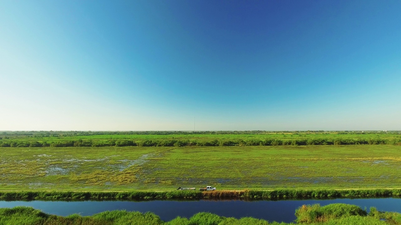 空中平移拍摄的绿色景观与河流和皮卡车对蓝天-河口，路易斯安那州视频素材