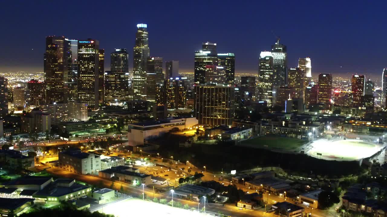 夜景中，城市中被照亮的现代建筑在天空的映衬下的航拍向前拍摄-洛杉矶，加利福尼亚视频素材