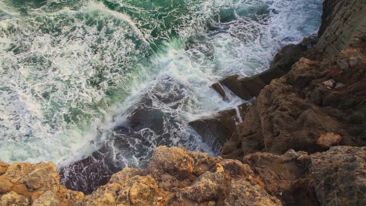 海浪冲击岩石海岸，绿色的水飞溅，创造白色的泡沫，从上面看，慢动作视频视频素材