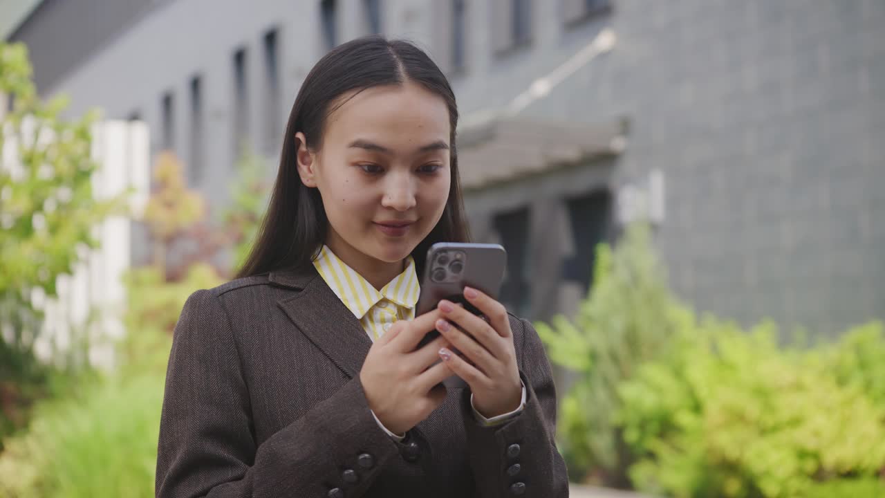 一个亚洲女人在外面玩手机。年轻的成年女性站在街上用智能手机。视频素材