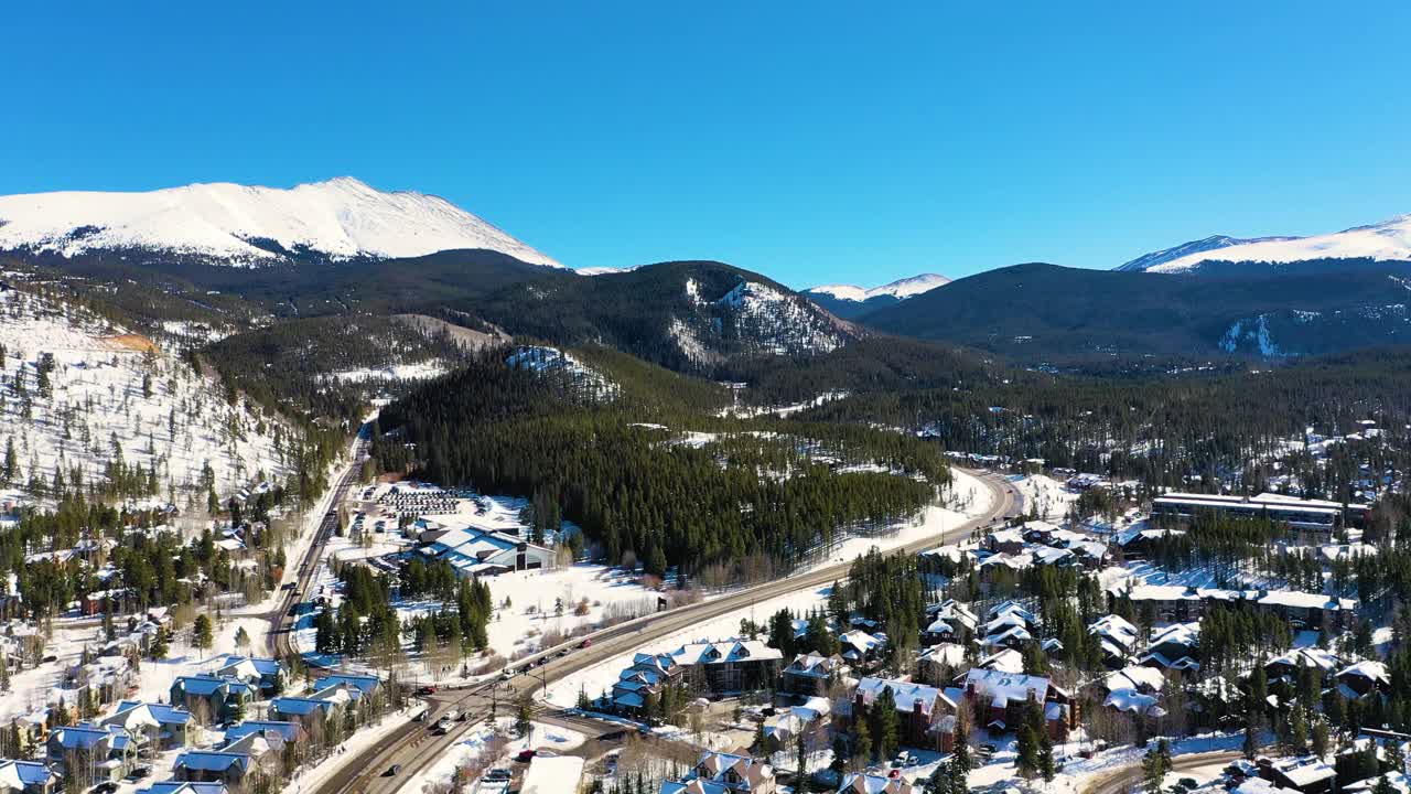 在美丽的布雷肯里奇科罗拉多山城，人们开车穿过松树林的道路上，无人机俯瞰白雪覆盖的房屋和山脉视频素材