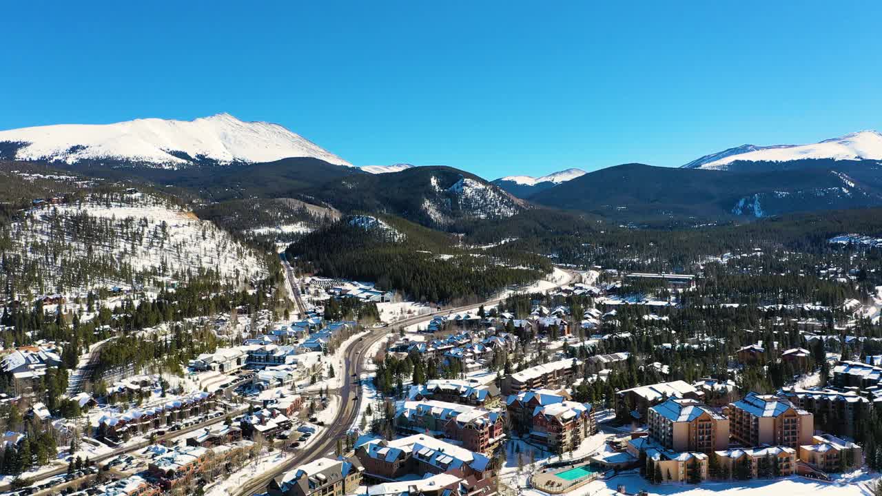 美丽的布雷肯里奇科罗拉多山城空中无人机观看积雪覆盖的房屋和山脉，人们开车穿过松树林的道路视频素材