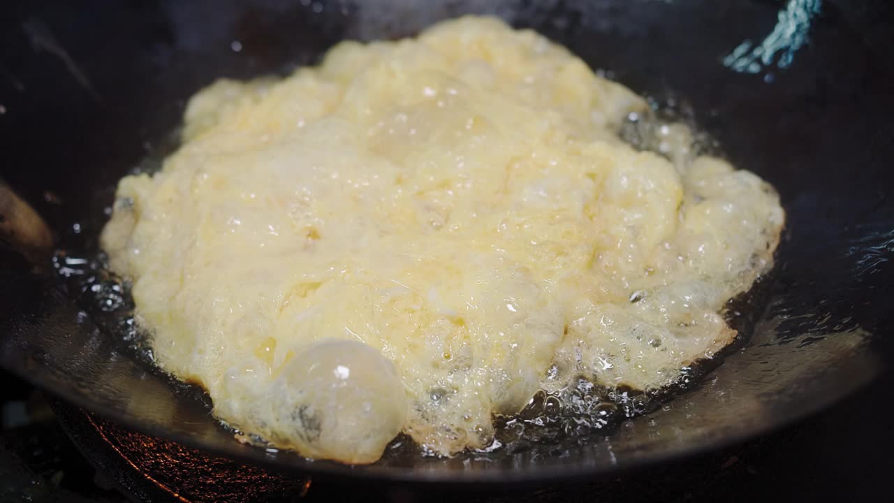 在热油煎锅中煎炸蓬松的蛋饼，泰国风味的食物，由打散的鸡蛋制成，泰国简单的街头小吃视频素材