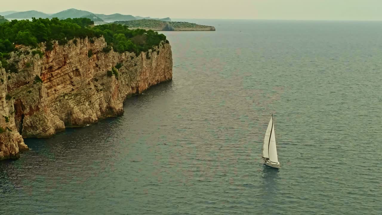 帆船在蓝色的大海上航行。高高的悬崖和高山。美丽的风景。波浪上的船。荒岛视频下载