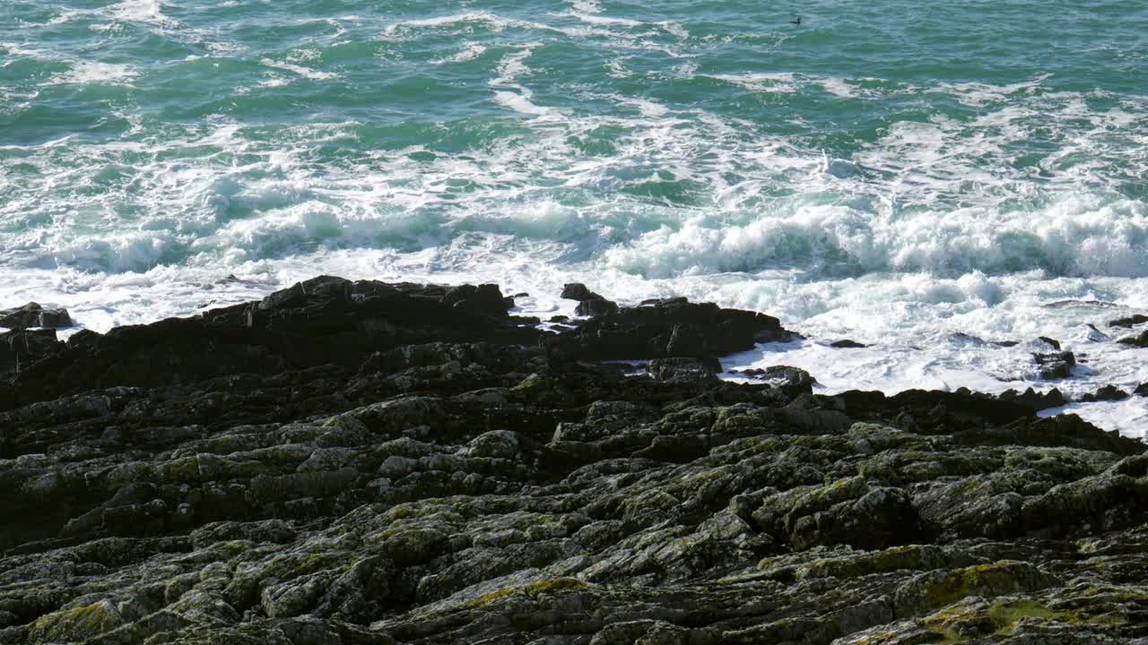 岩石嶙峋的海岸线，黑暗嶙峋的岩石勇敢地承受着海浪不断的冲击。深蓝绿的大海，海浪激起耀眼的白色泡沫。锅视频素材