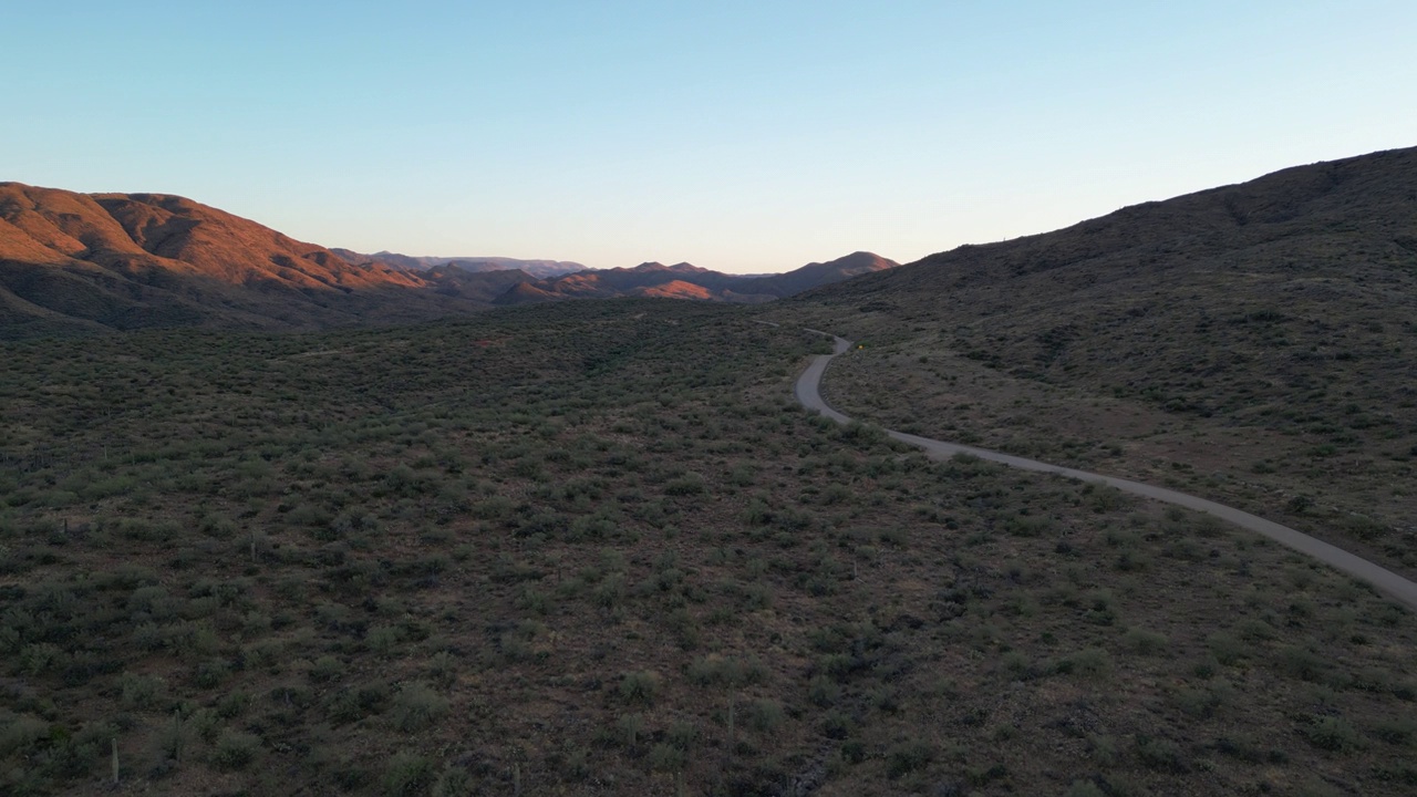 空旷的沙漠道路在一个巨大的沙漠山谷中间，群山被早晨的日出照亮视频素材