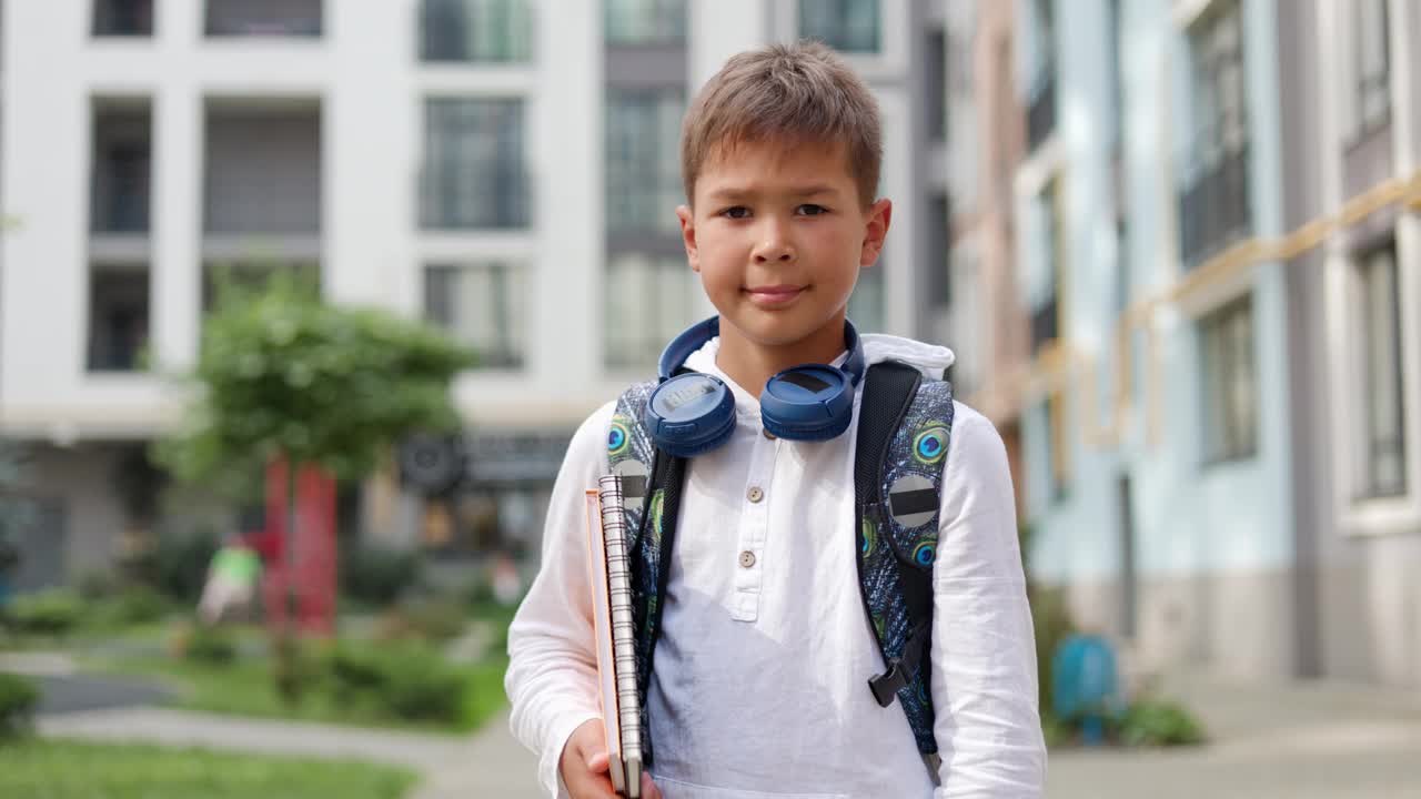 一个积极向上的青少年，准备好迎接新的一天的学校生活，他站在学校外面，背着背包，自信地看着镜头。学校与儿童概念。视频素材